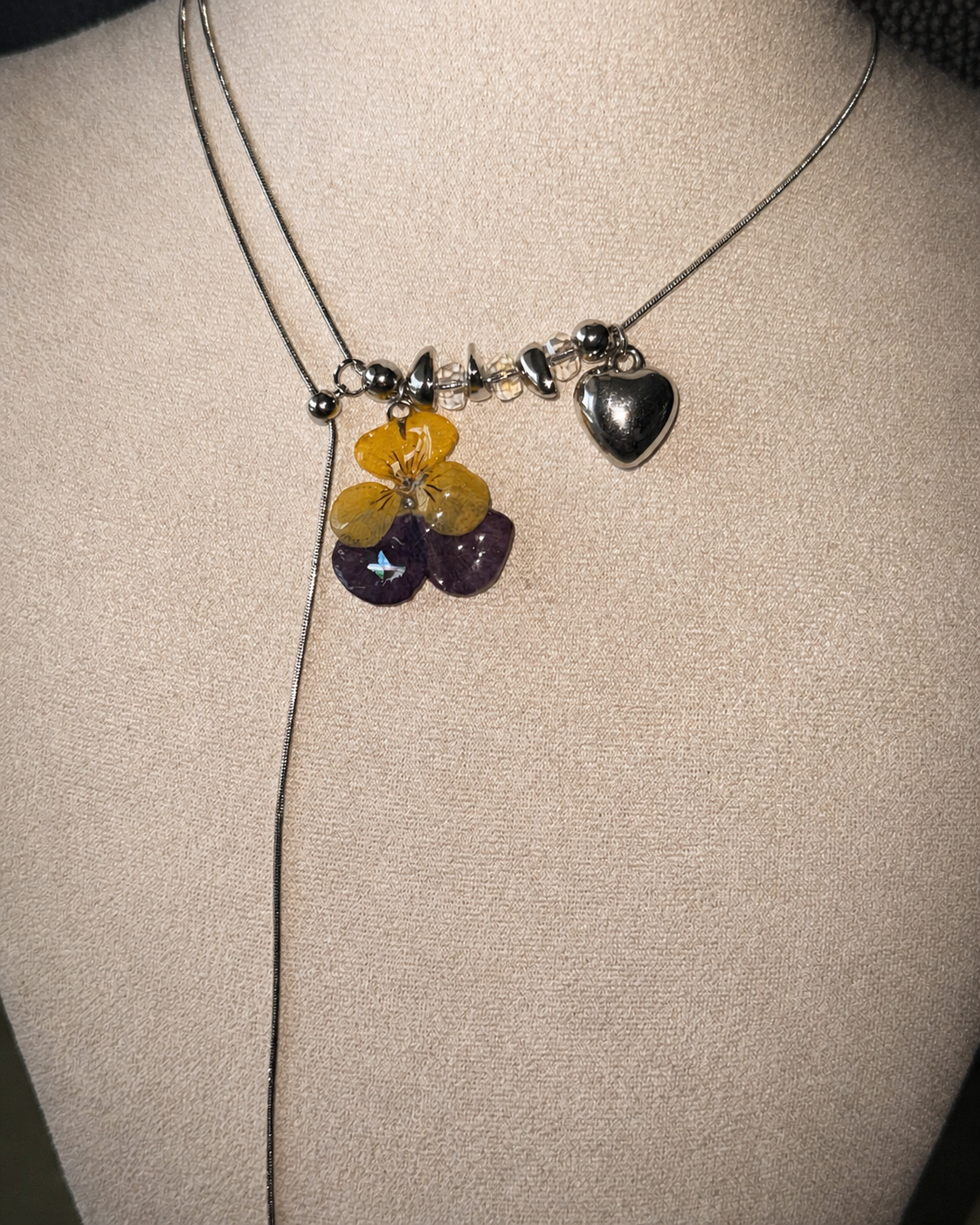 Full-length flash view of the adjustable pansy lariat necklace on a cream display, Pansy Heart Adjustable Lariat Necklace botanical jewellery by Terra Decode