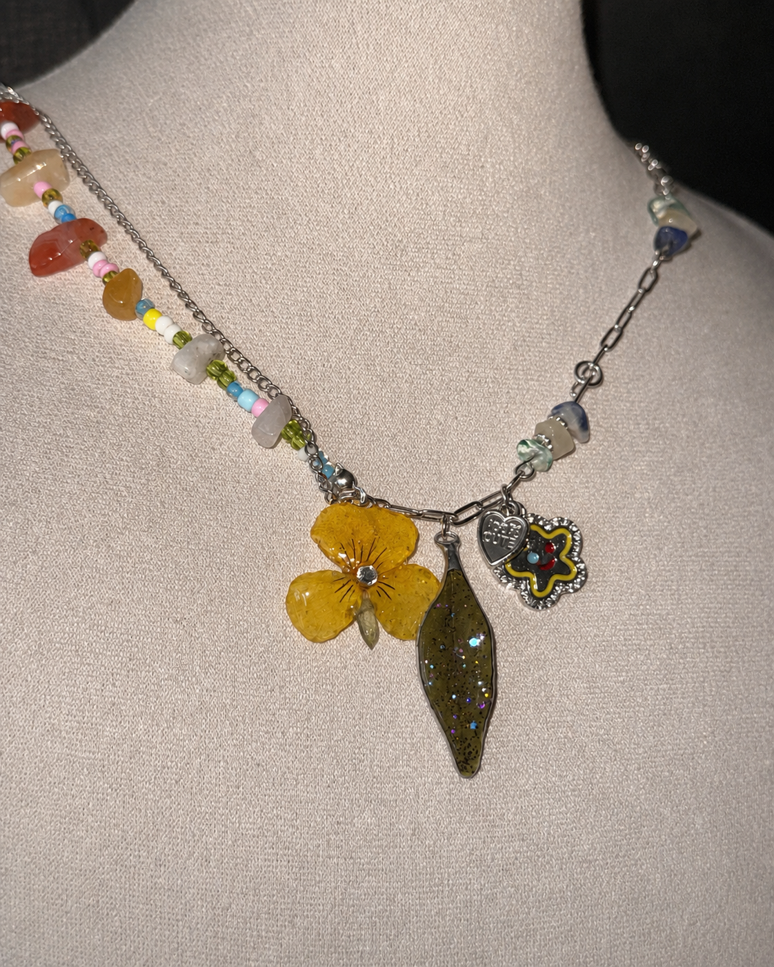 Full necklace view on a cream jewellery bust showing mixed chain and charms, Yellow Pansy & Nandina Leaf Y2K Charm Necklace botanical jewellery by Terra Decode