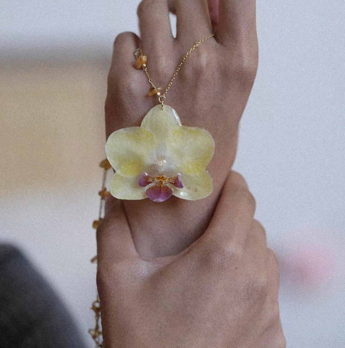 Butter yellow preserved orchid pendant necklace worn on hand by Terra Decode