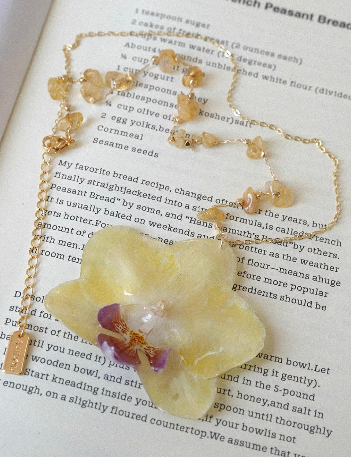 Butter yellow orchid pendant necklace with gold-tone beaded chain on book page by Terra Decode