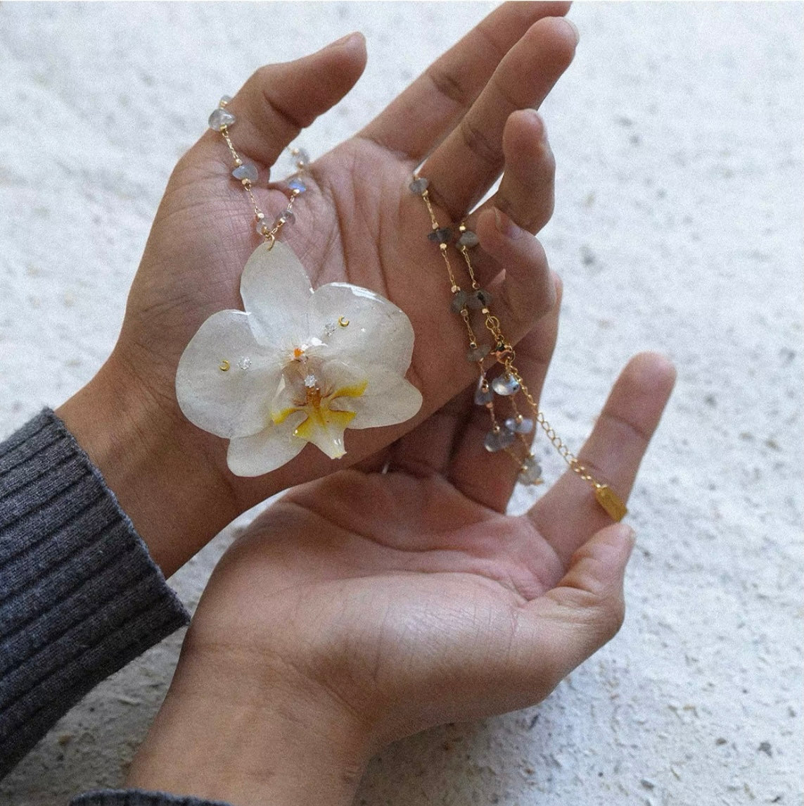 Ivory white orchid flower pendant necklace held in hand by Terra Decode