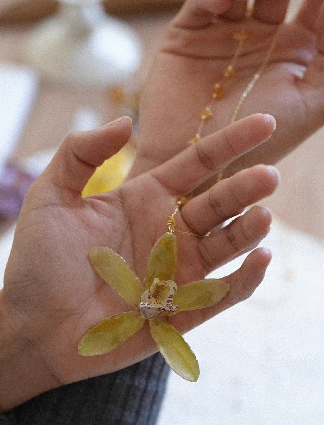 Olive green orchid pendant necklace held in hand by Terra Decode