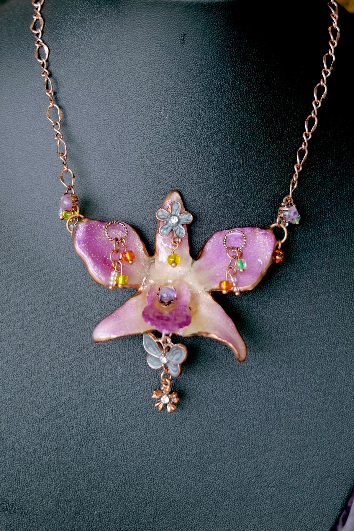 Detail of a purple Dendrobium orchid pendant with rose-gold metal, crystals and small floral charms.