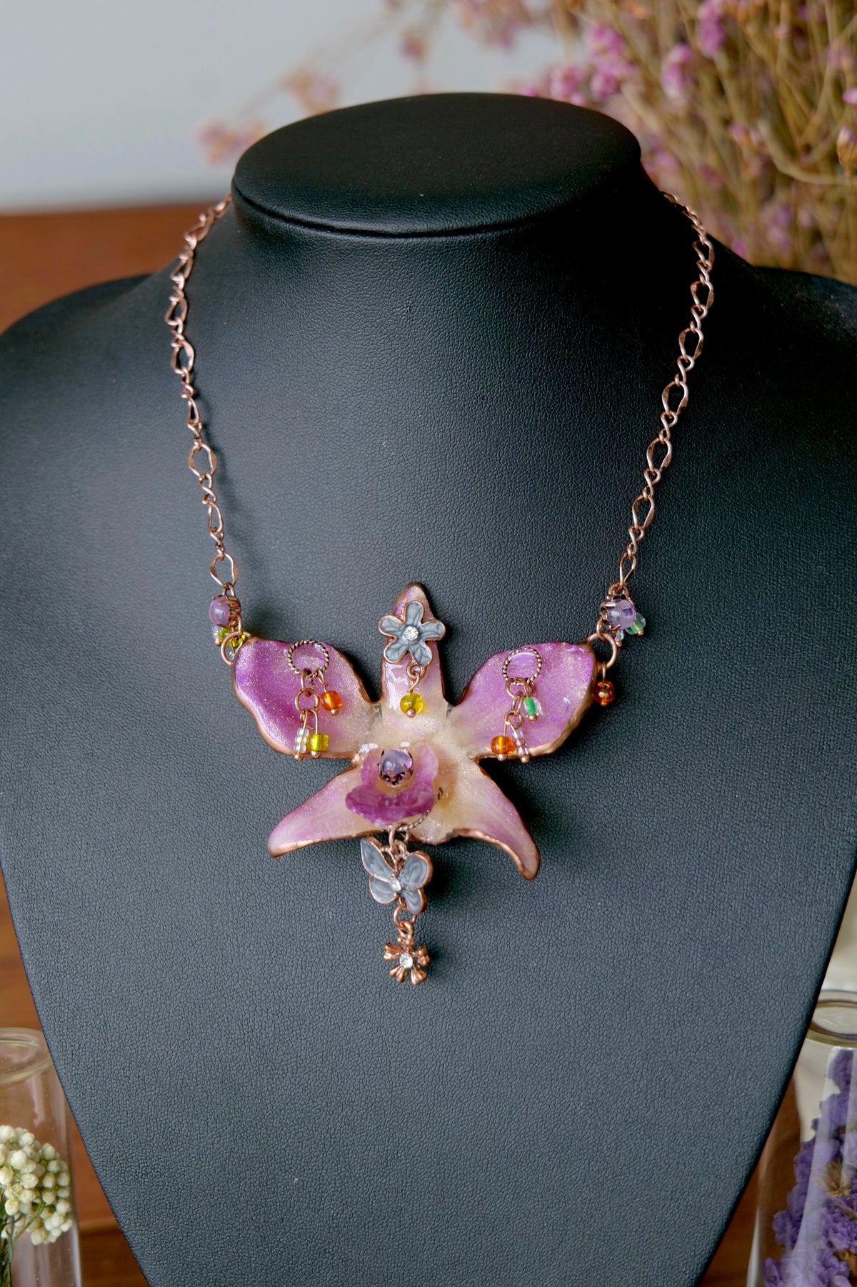 Close view of preserved purple Dendrobium orchid petals and dangling vintage-inspired charms.