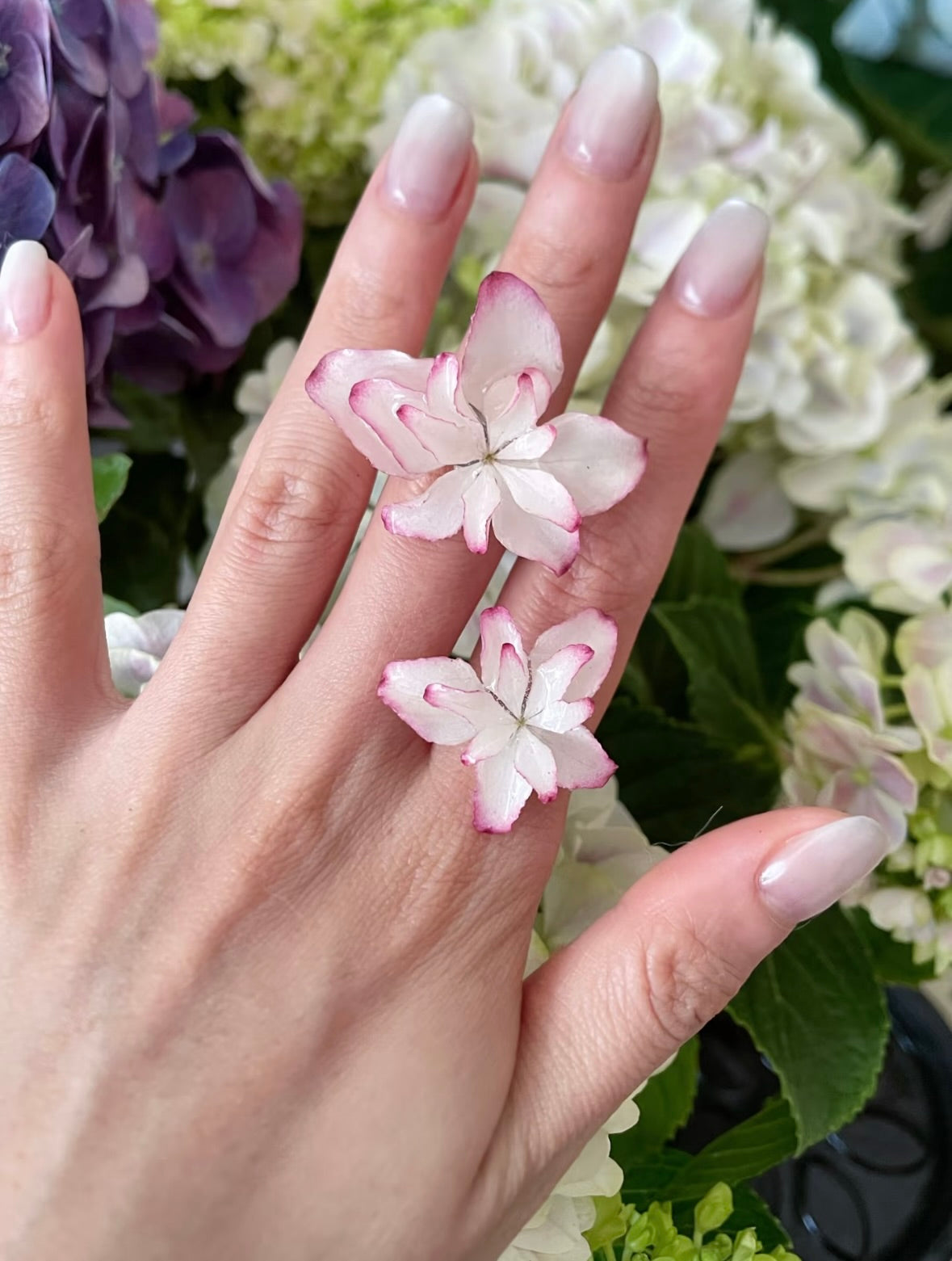 Soft pink hydrangea ring with resin petals worn among white and purple hydrangeas by Terra Decode