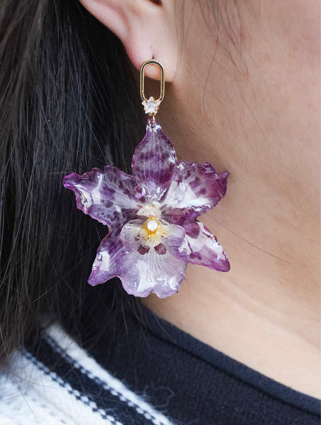 Spotted purple orchid earrings with resin petals and gold-tone hooks worn on ear by Terra Decode