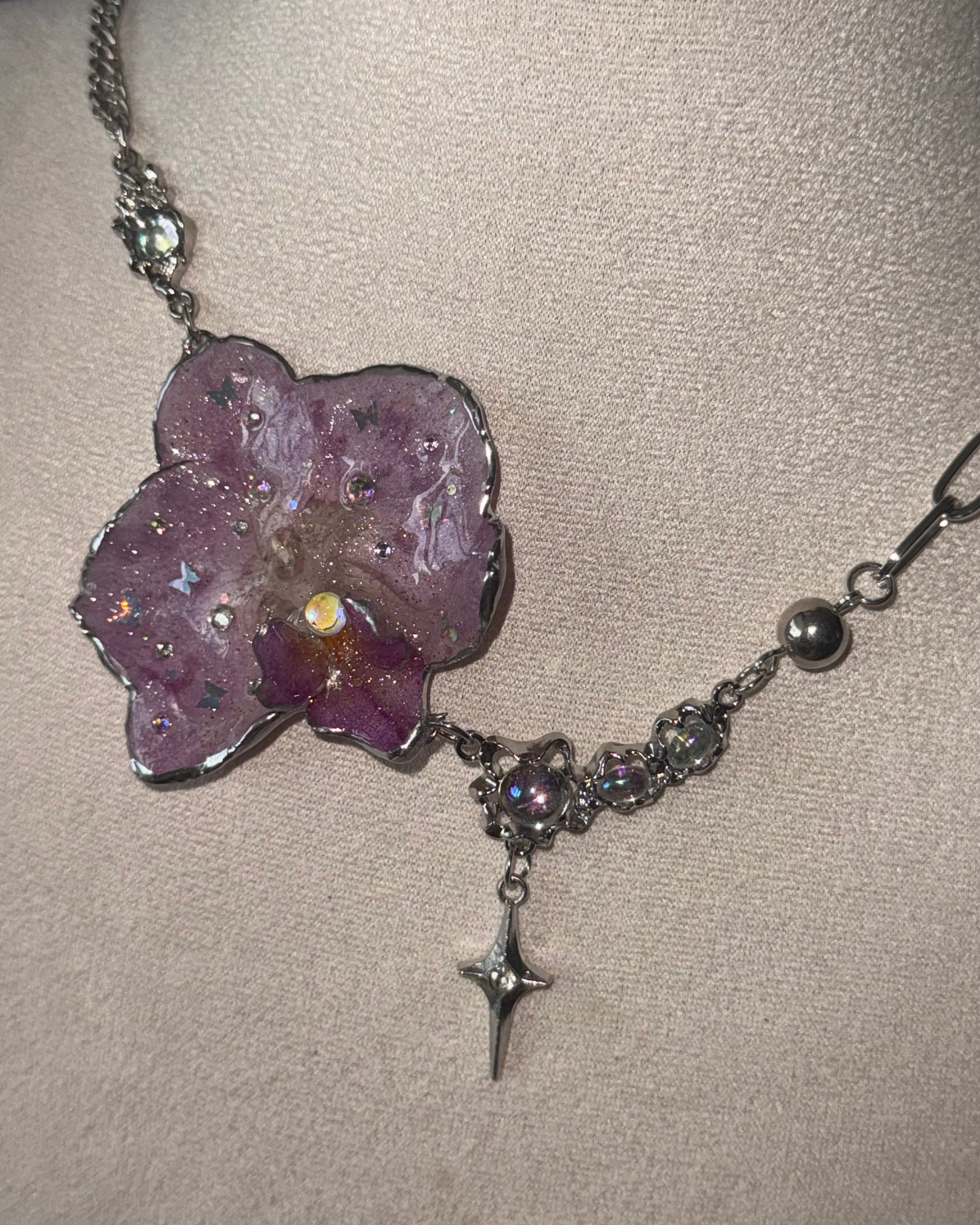 Reflective detail of lilac phalaenopsis pendant, iridescent accents and silver-toned star