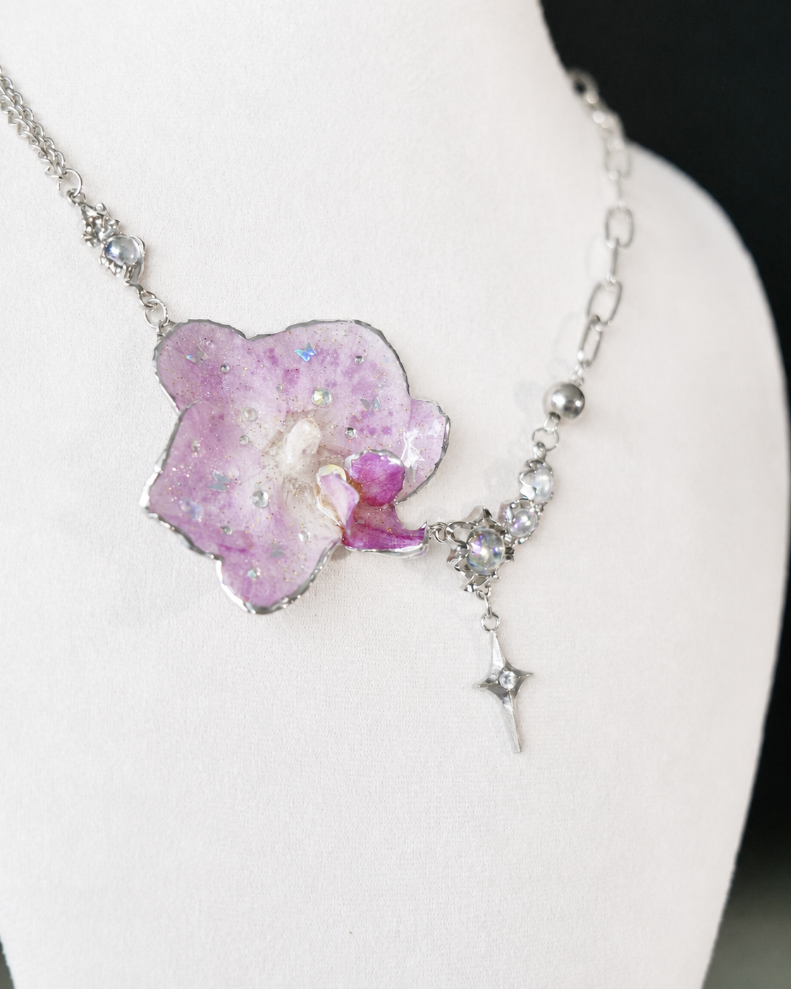 Angled view of the asymmetric lilac orchid pendant and iridescent stone accents, Lilac Phalaenopsis Moonstone-Style Star-Drop Necklace botanical jewellery by Terra Decode