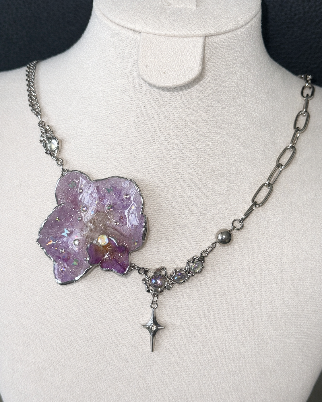 Bright flash view of the complete asymmetric orchid necklace on a cream jewellery bust, Lilac Phalaenopsis Moonstone-Style Star-Drop Necklace botanical jewellery by Terra Decode