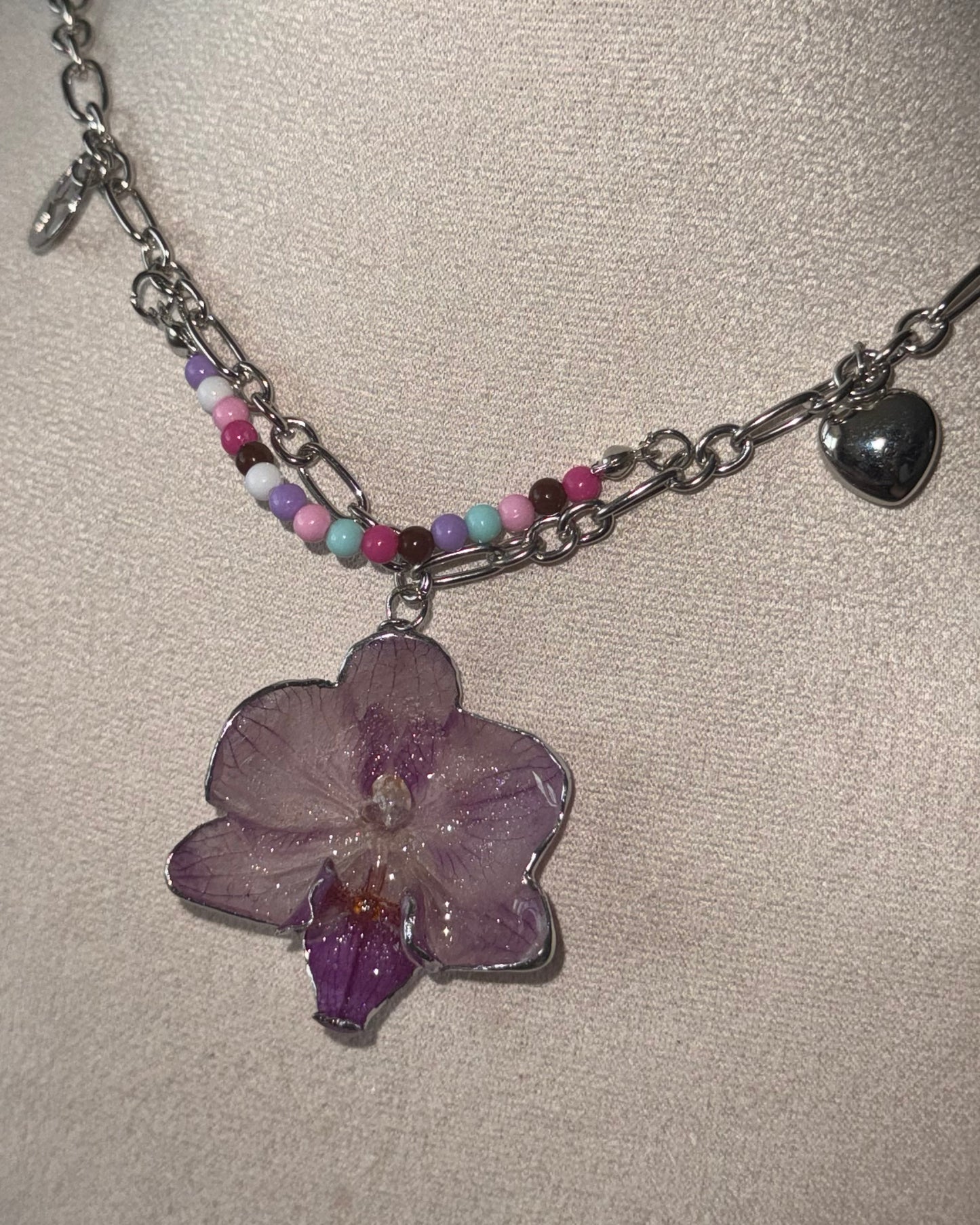 Reflective detail of lilac phalaenopsis pendant and layered pastel beads