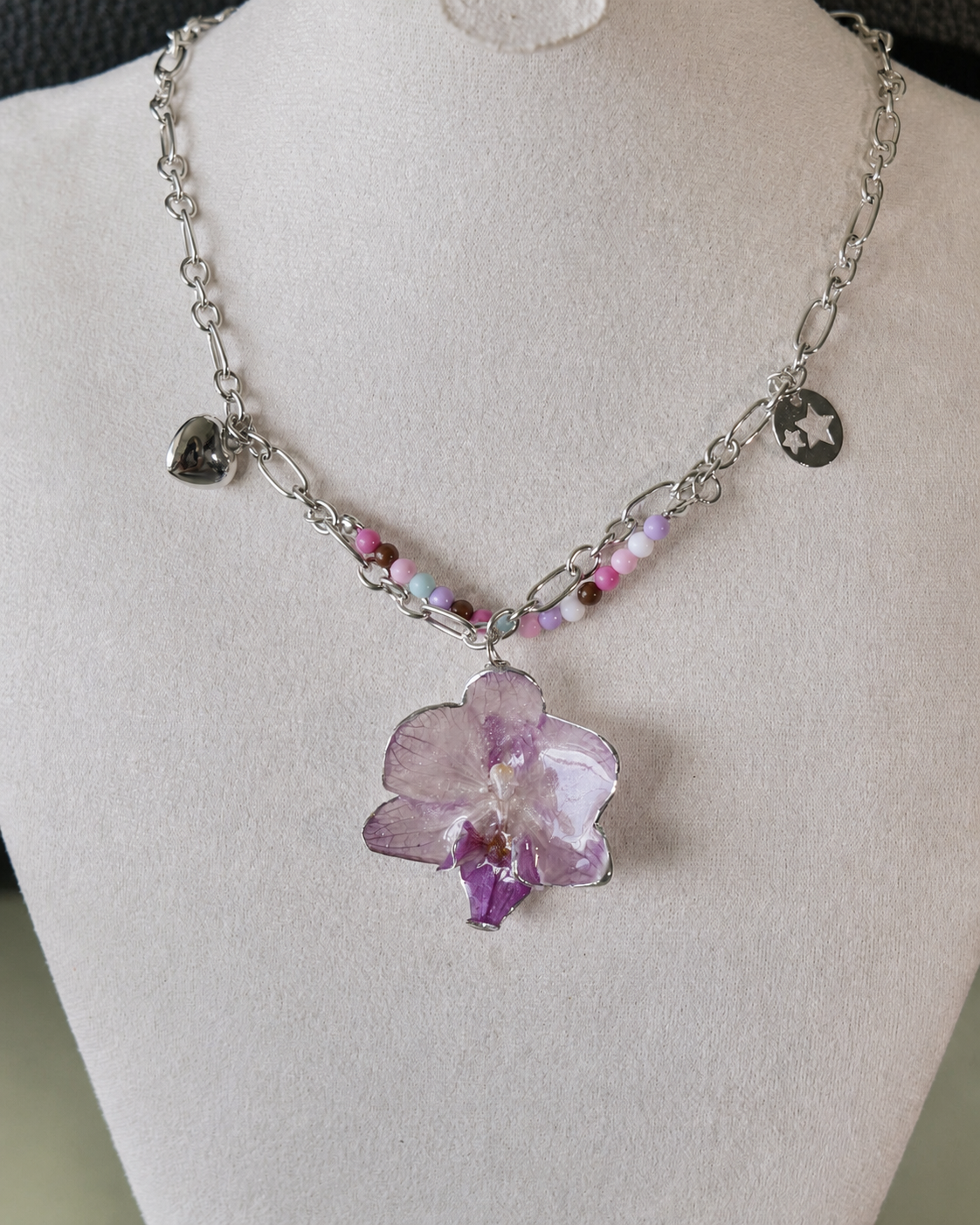 Angled view of the preserved lilac orchid pendant and layered pastel bead strand, Lilac Phalaenopsis Pastel Bead Charm Necklace botanical jewellery by Terra Decode