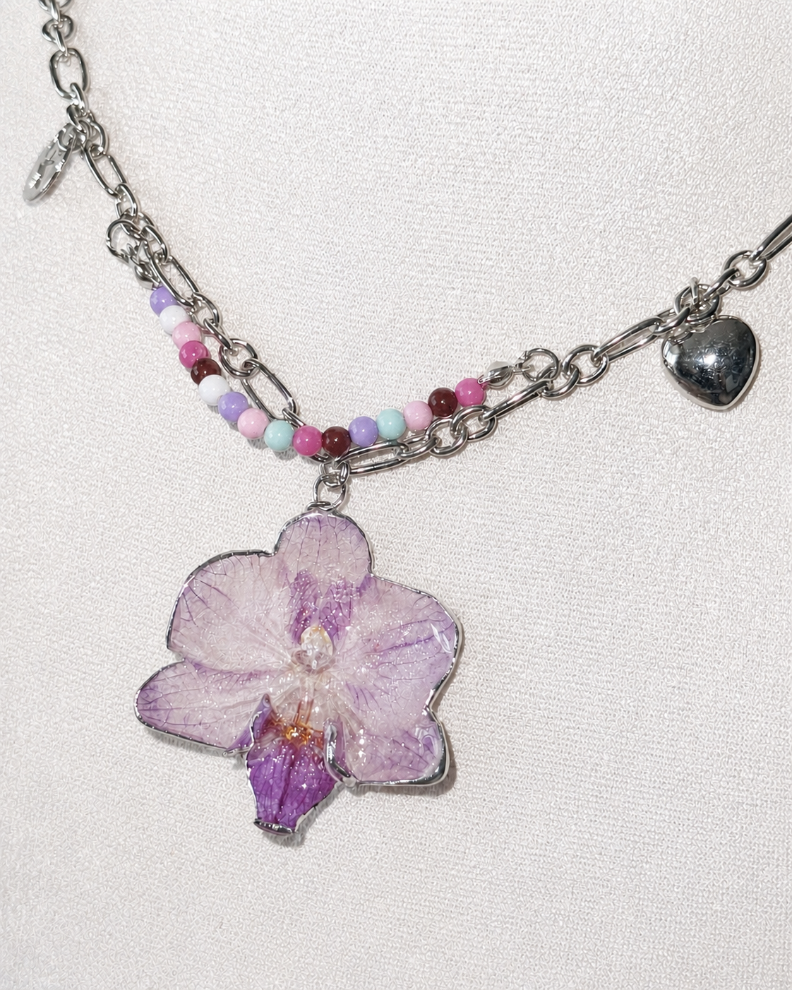 Bright flash detail of the orchid pendant, pastel beads and heart charm, Lilac Phalaenopsis Pastel Bead Charm Necklace botanical jewellery by Terra Decode