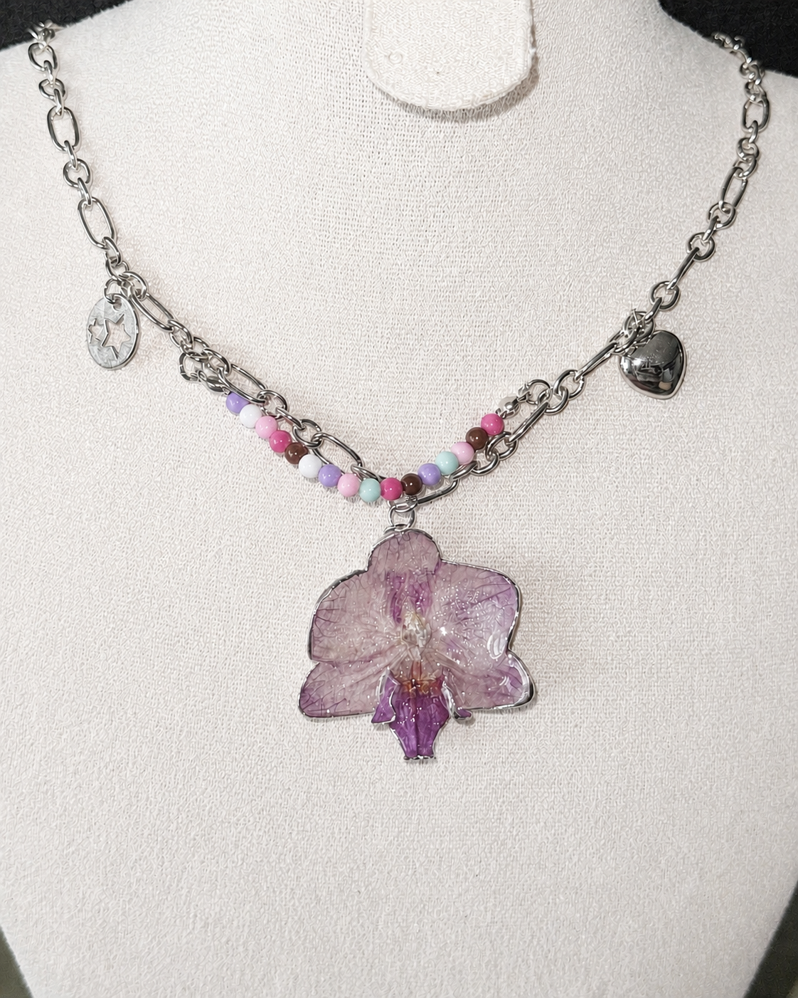 Full flash view of the Lilac Phalaenopsis Pastel Bead Charm Necklace on a cream display, Lilac Phalaenopsis Pastel Bead Charm Necklace botanical jewellery by Terra Decode