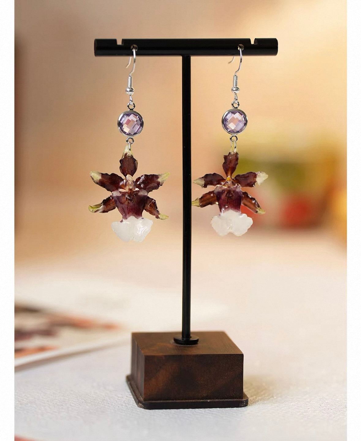 Deep plum oncidium orchid earrings with resin flower petals on a display stand by Terra Decode