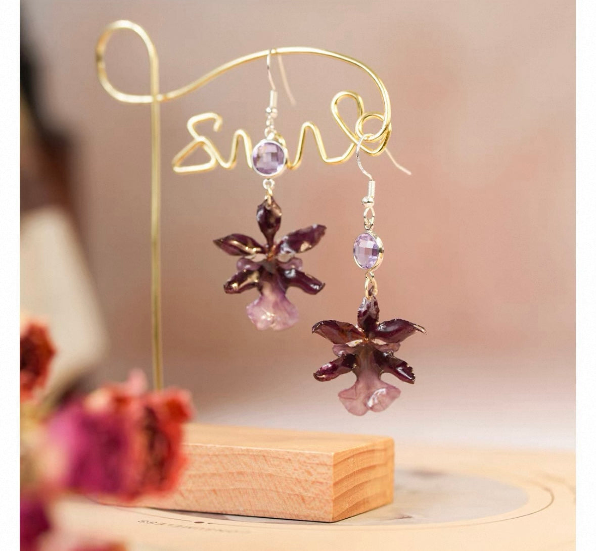 Deep plum oncidium orchid earrings with resin petals on a gold display stand by Terra Decode