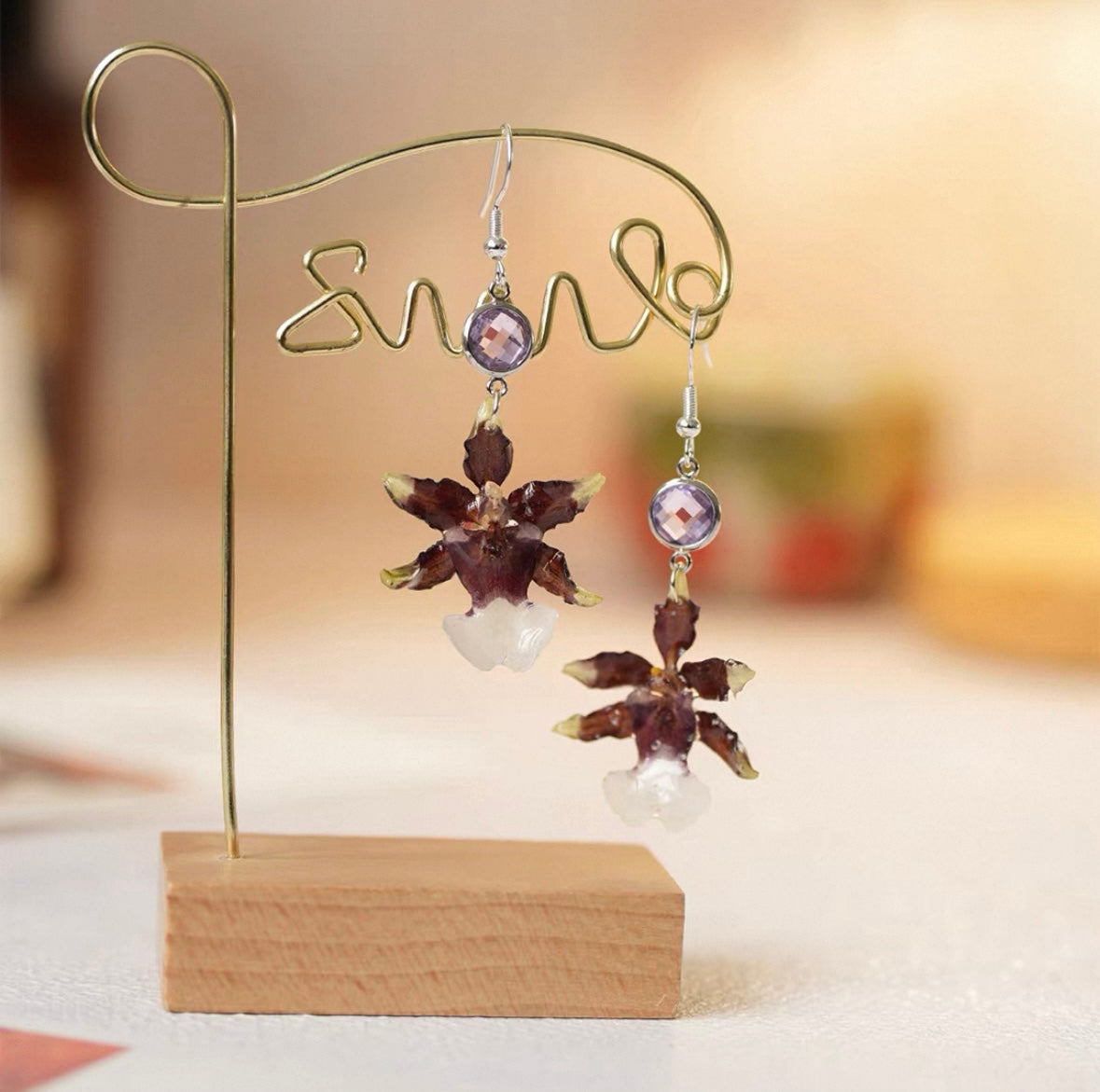 Deep plum oncidium orchid drop earrings with bead details on a wooden display stand by Terra Decode