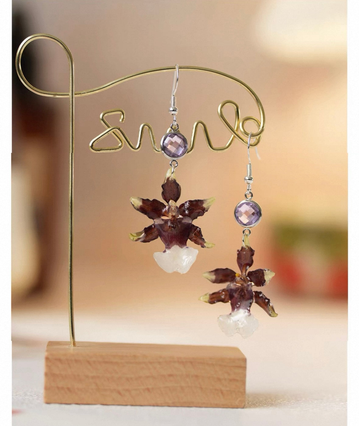 Deep plum oncidium orchid drop earrings with white bead drops on a wooden display stand by Terra Decode