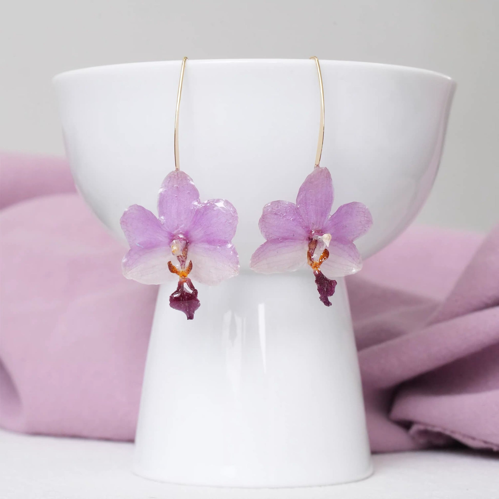 Soft purple orchid ear hook earrings with resin petals displayed on a white cup by Terra Decode