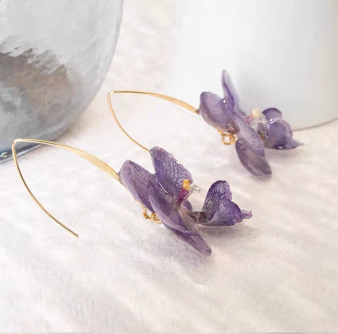 Soft purple orchid ear hook earrings with resin petals arranged on fabric by Terra Decode
