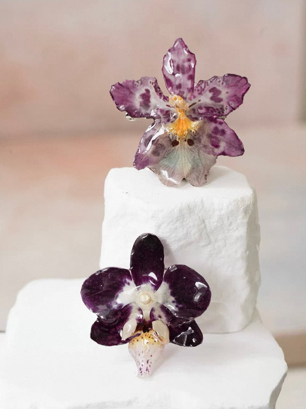 Soft purple and deep plum orchid brooches with resin petals displayed on white plaster stands by Terra Decode
