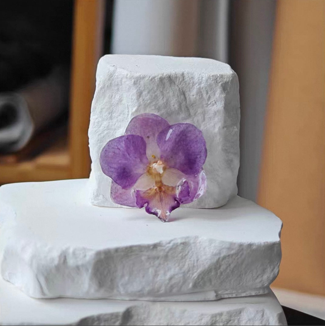 Soft purple orchid brooch with resin petals displayed on a white plaster block by Terra Decode
