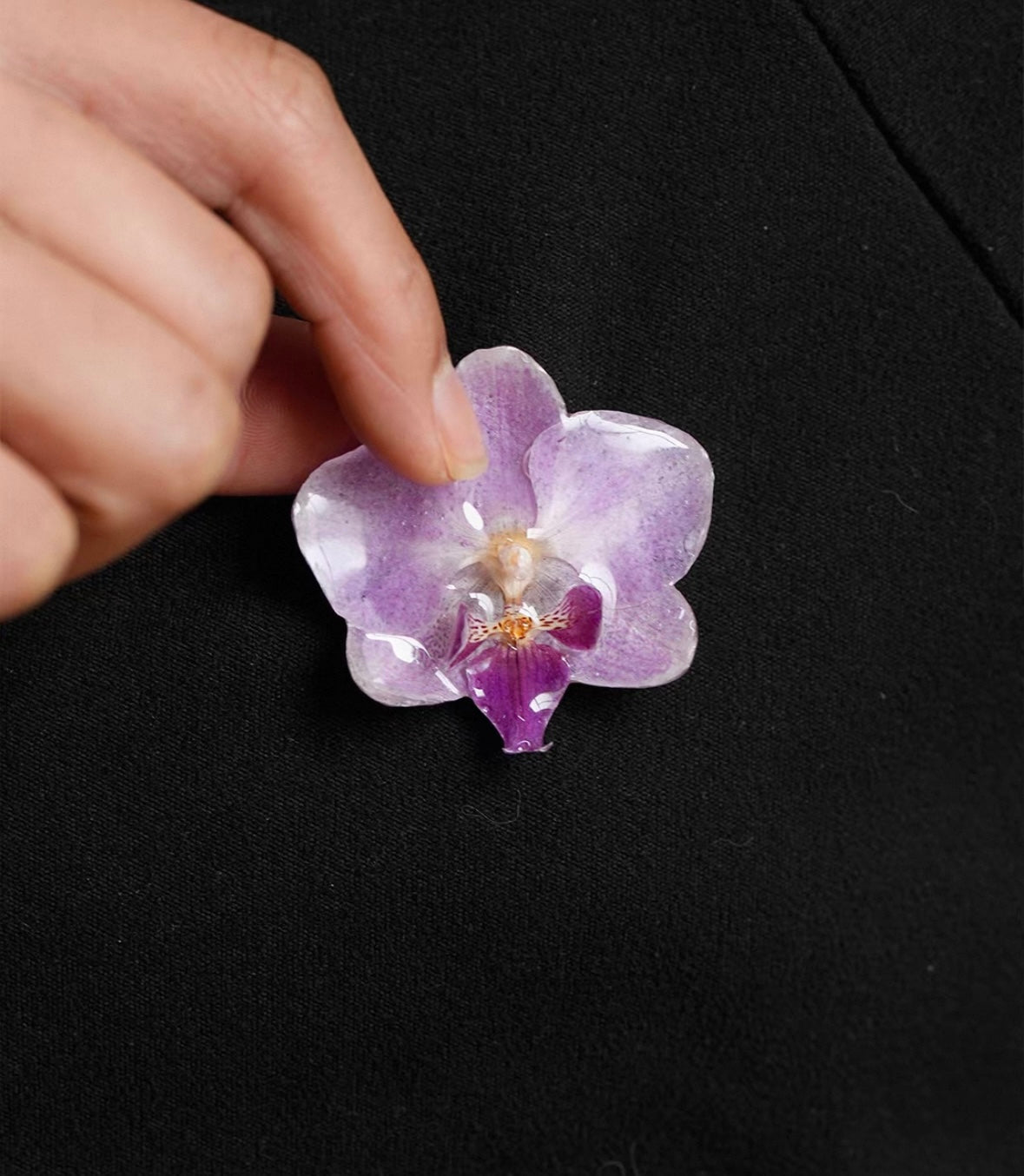 Soft purple orchid brooch with resin petals held against black fabric by Terra Decode