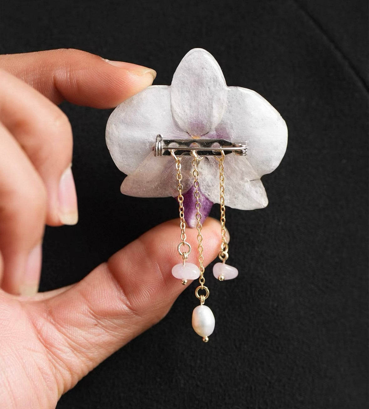 White pearl detail orchid brooch with resin petals, pin back and pearl-like drops held in hand by Terra Decode