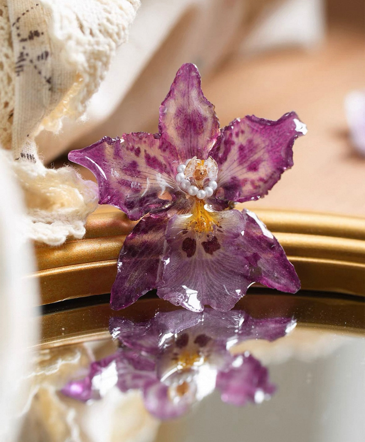 Speckled purple orchid brooch with resin petals and pearl-like centre on a mirror by Terra Decode