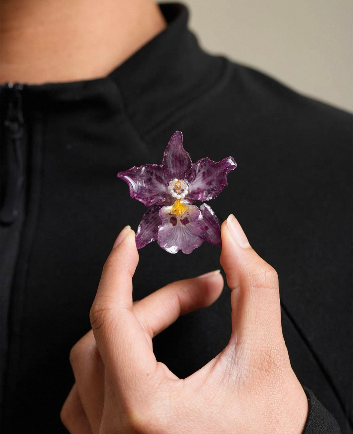 Speckled purple orchid brooch with resin petals held near black fabric by Terra Decode