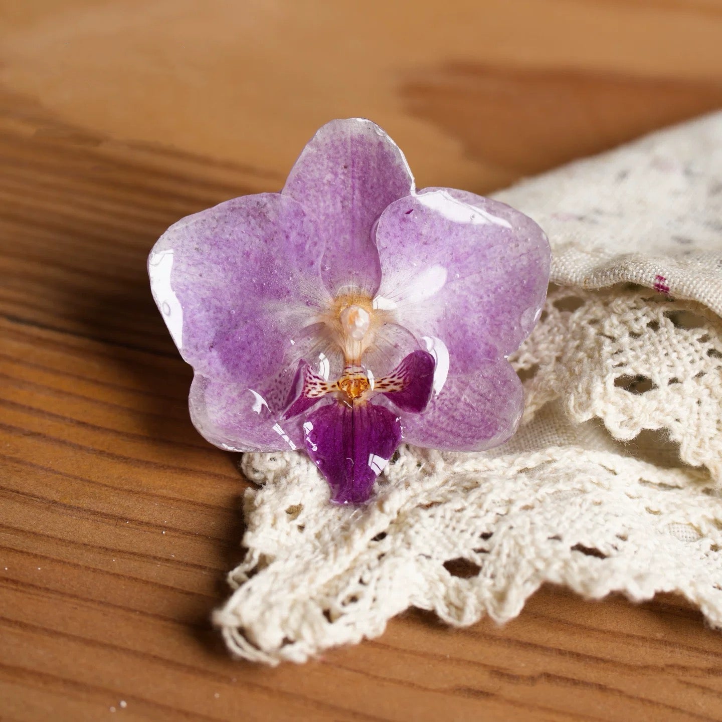 Soft purple orchid brooch with resin petals displayed on lace and wood by Terra Decode
