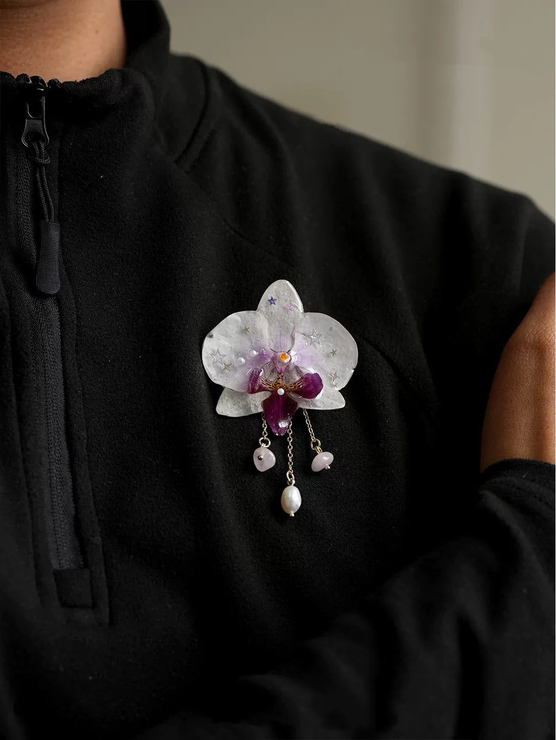 White pearl detail orchid brooch with resin petals and pearl-like drops worn on black top by Terra Decode