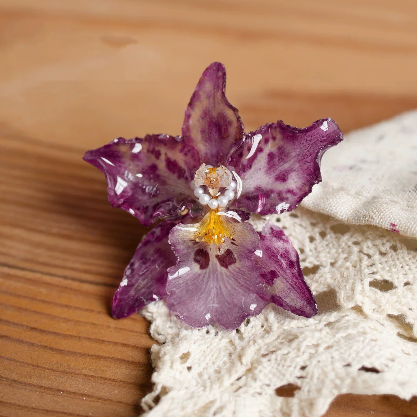 Speckled purple orchid brooch with resin petals and pearl-like centre on wood and lace by Terra Decode