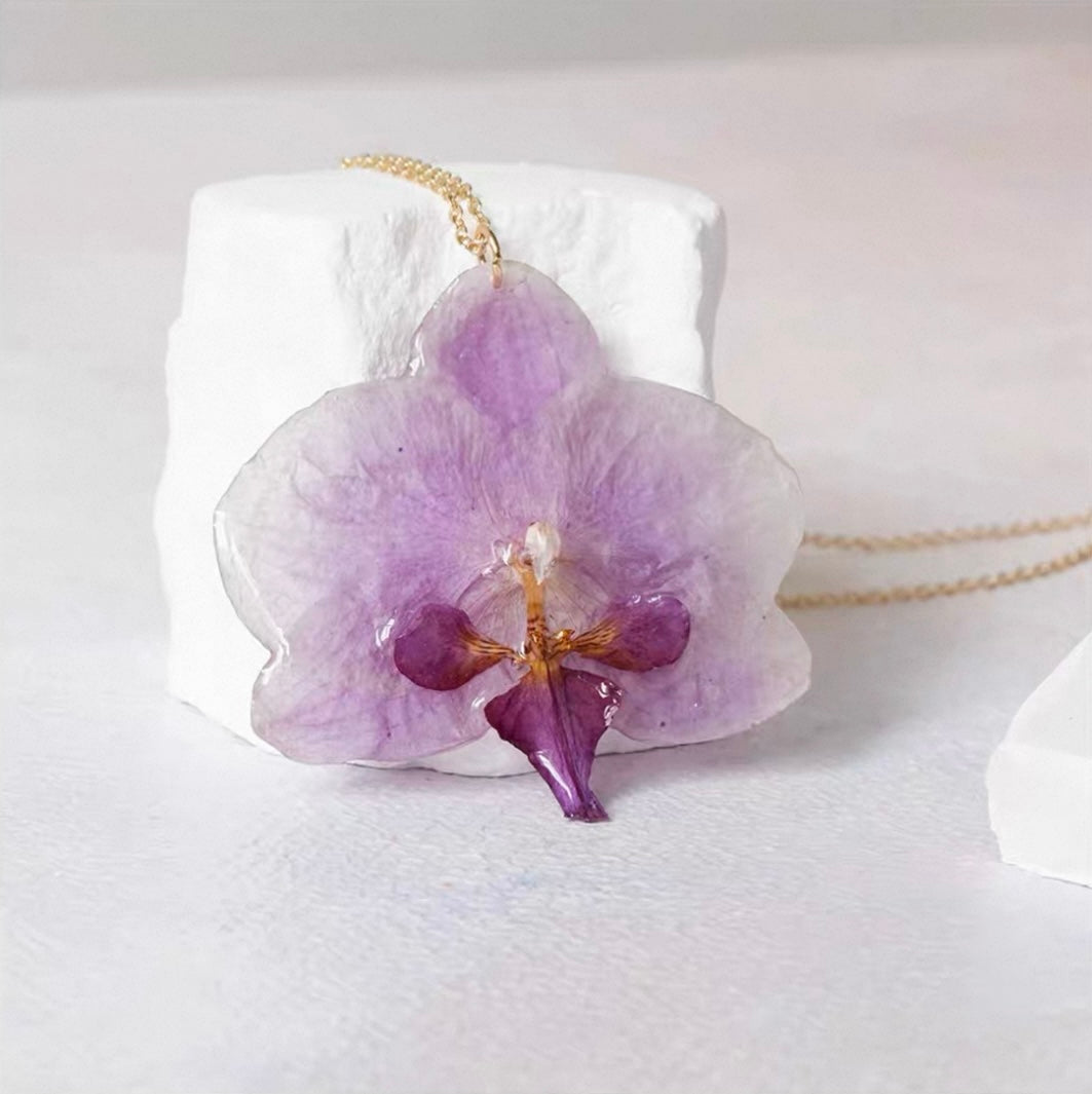 Soft purple orchid necklace with resin flower pendant displayed on a white plinth by Terra Decode