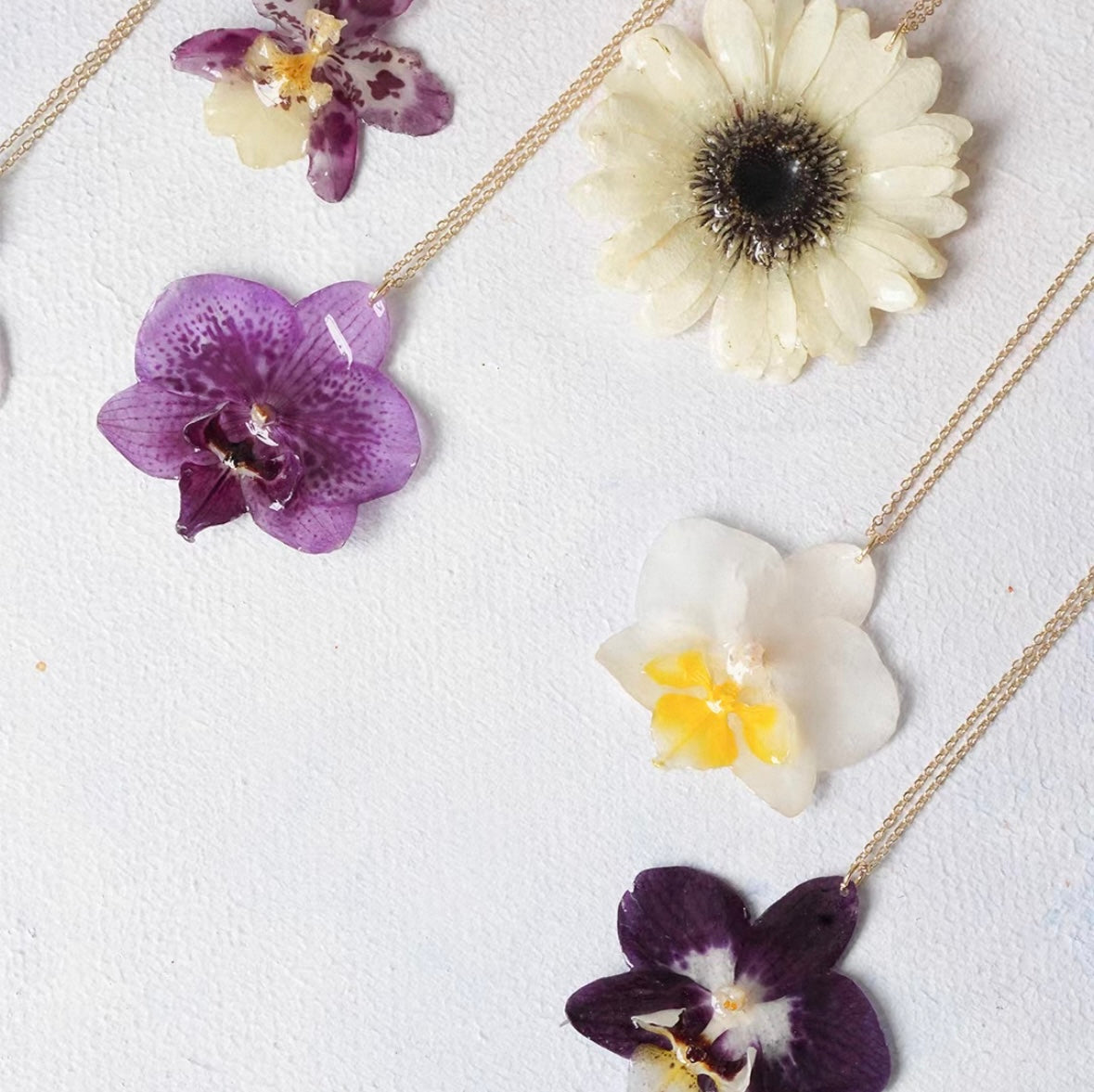 Orchid flower pendant necklaces with resin petals and gold-tone chains displayed together by Terra Decode