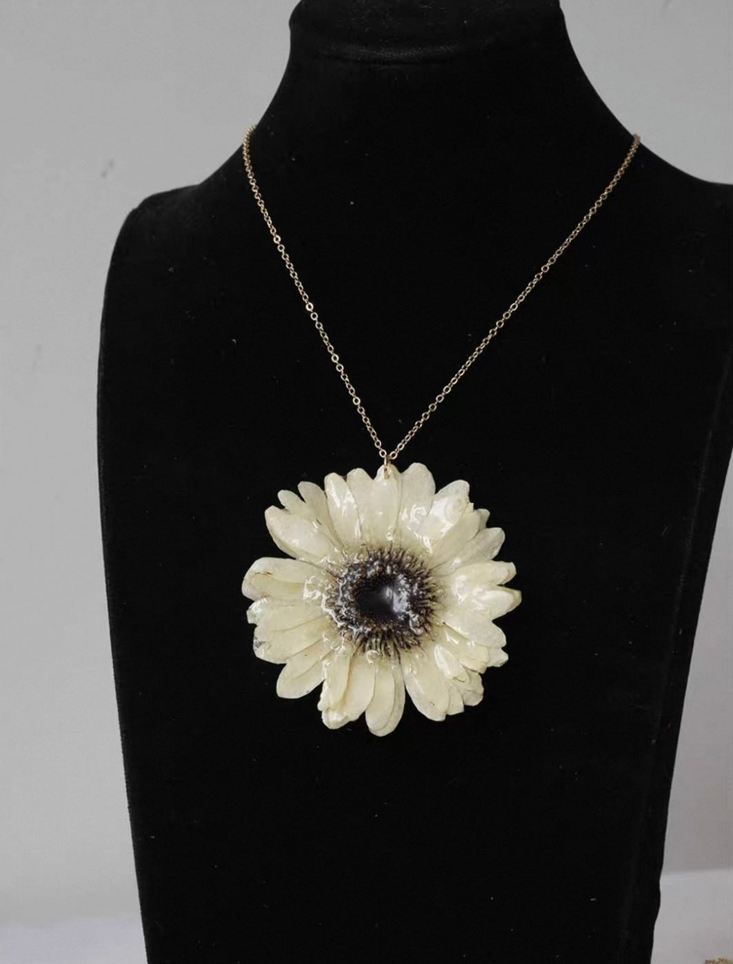 Cream daisy-style flower pendant necklace with resin petals on a black bust by Terra Decode