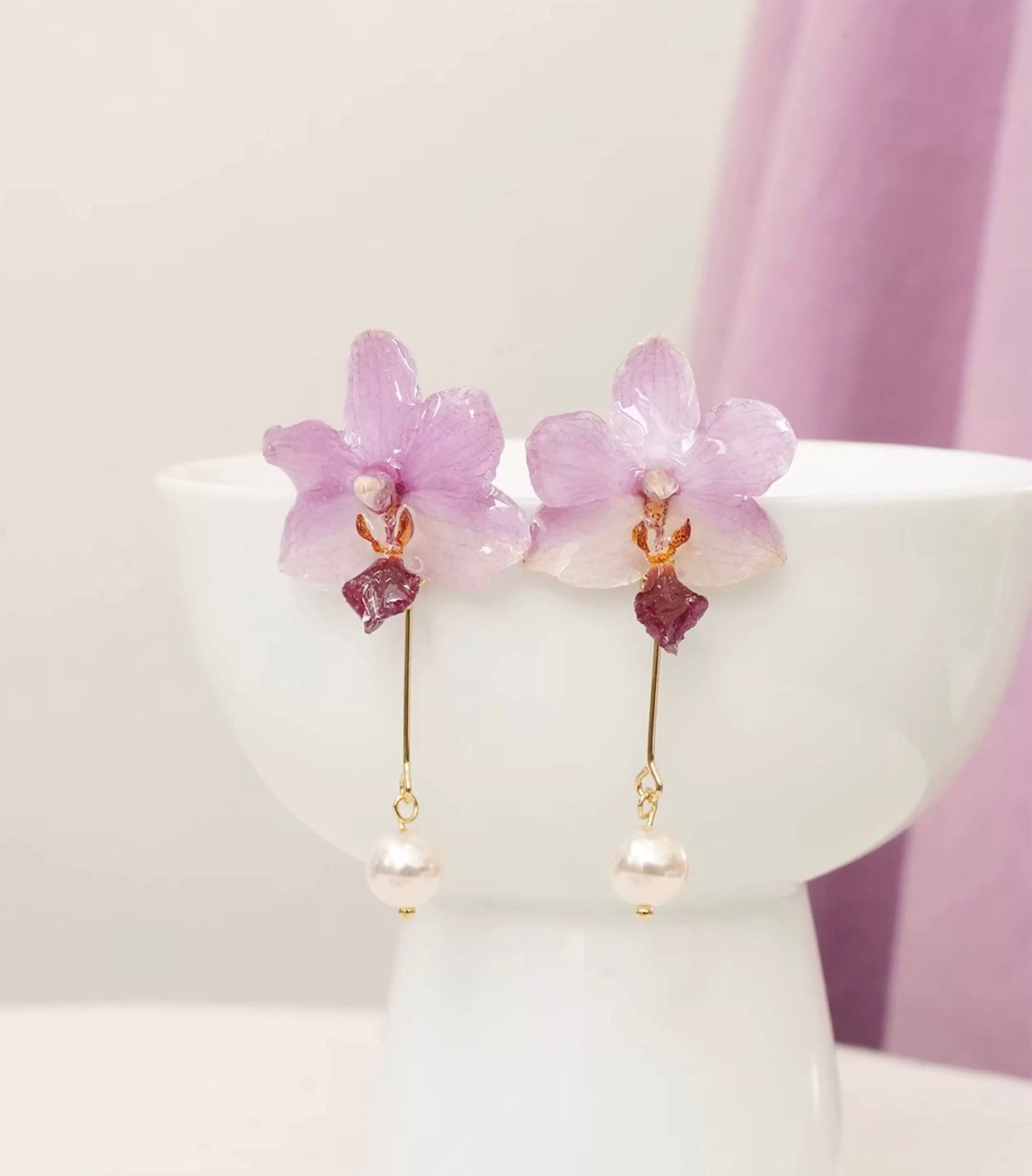 Lavender purple orchid earrings with resin petals displayed on a white cup by Terra Decode