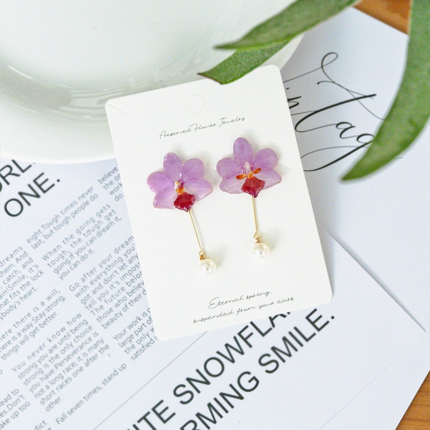 Soft pink orchid pearl drop earrings with resin petals on a printed page by Terra Decode