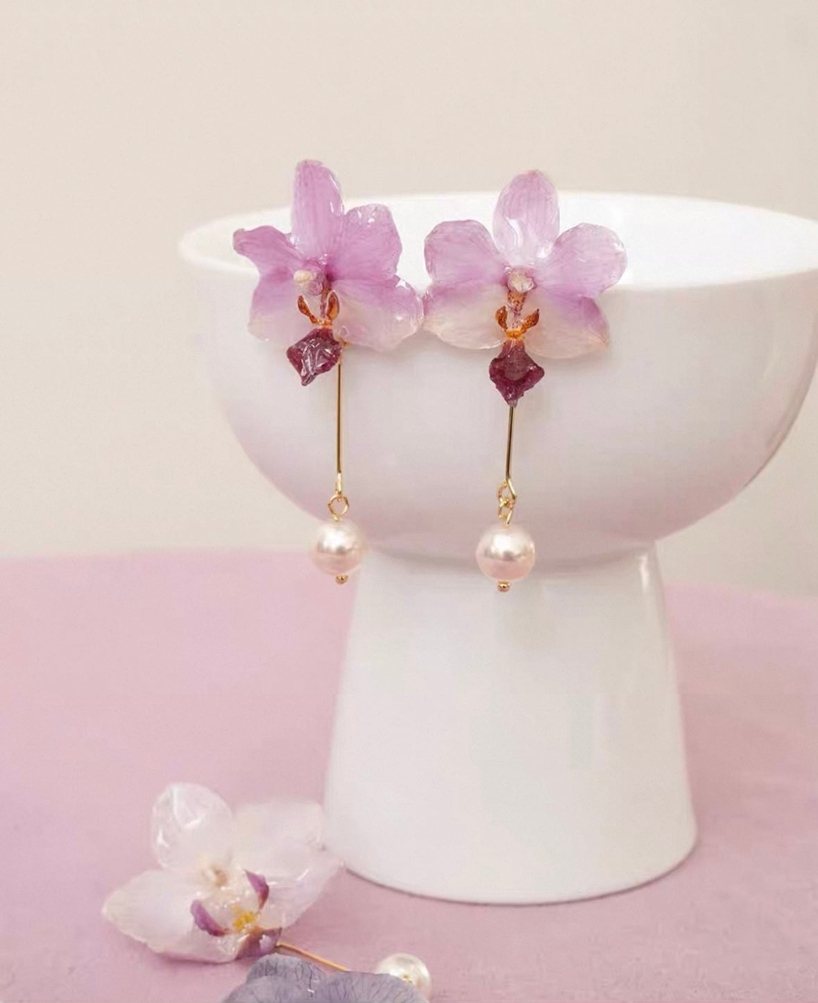 Soft pink orchid pearl drop earrings with resin petals displayed on a white ceramic cup by Terra Decode