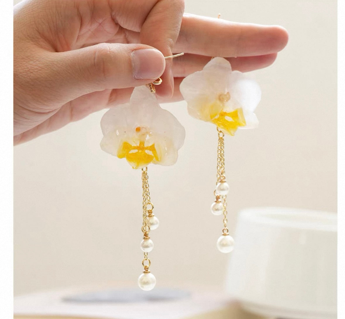 Cream white orchid earrings with resin petals, chain detail and pearl-like drops by Terra Decode