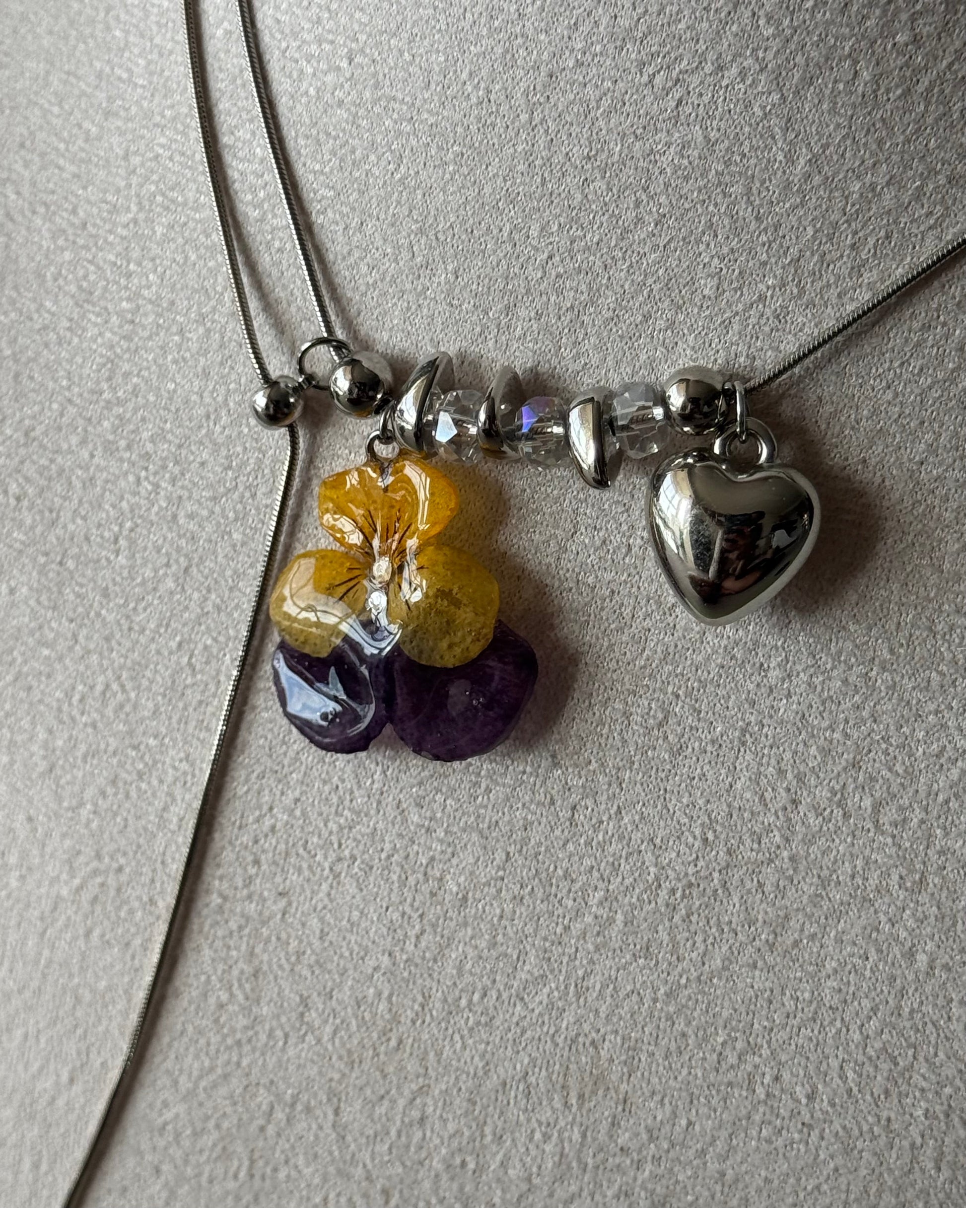 Close-up of preserved pansy pendant and silver-toned heart charm