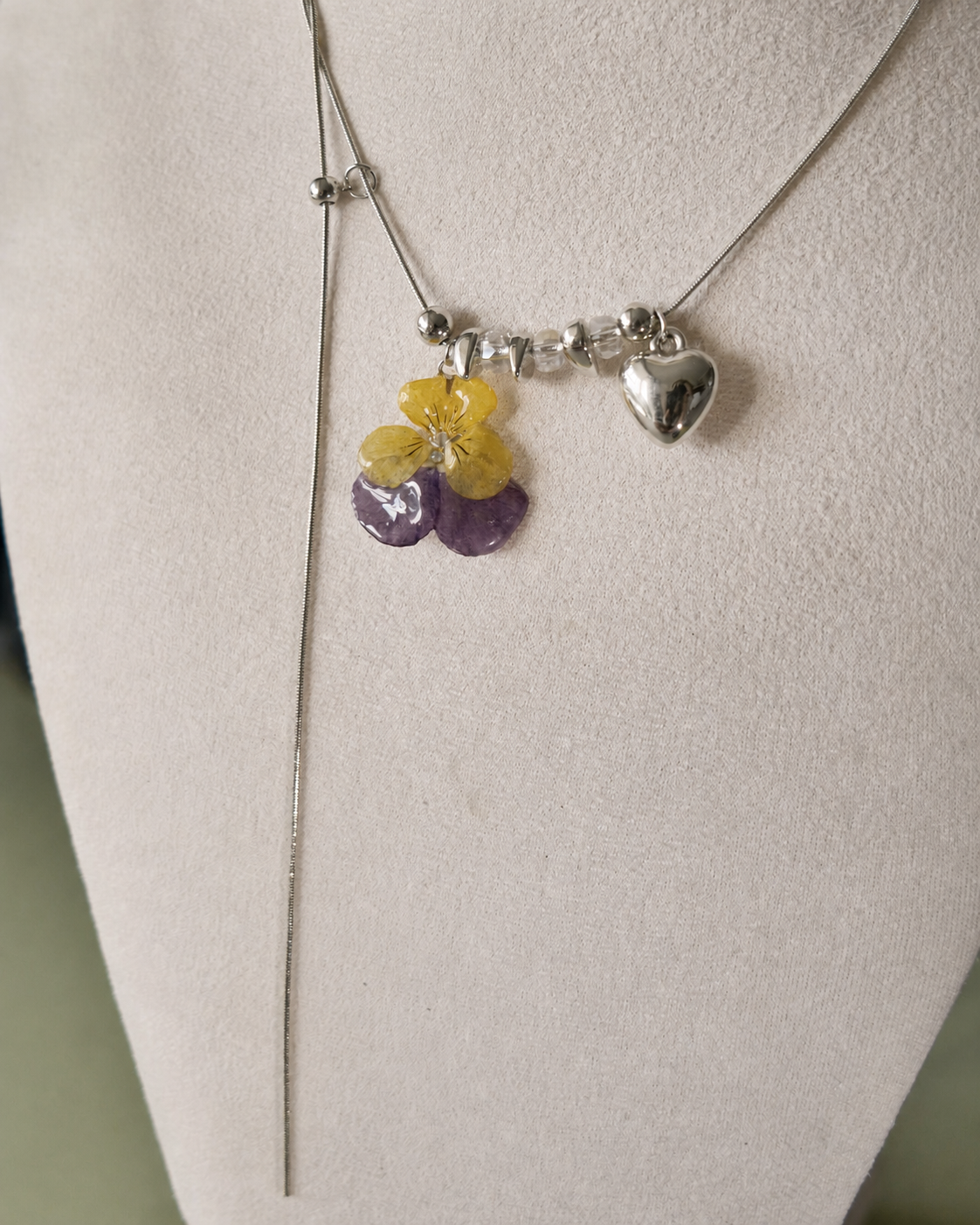 Angled display view of the preserved pansy lariat necklace and silver-toned heart charm, Pansy Heart Adjustable Lariat Necklace botanical jewellery by Terra Decode