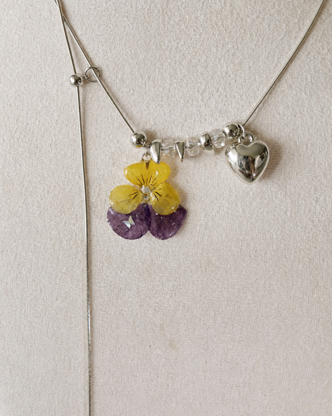 Close view of the real pansy resin pendant, clear beads and adjustable silver-toned chain, Pansy Heart Adjustable Lariat Necklace botanical jewellery by Terra Decode