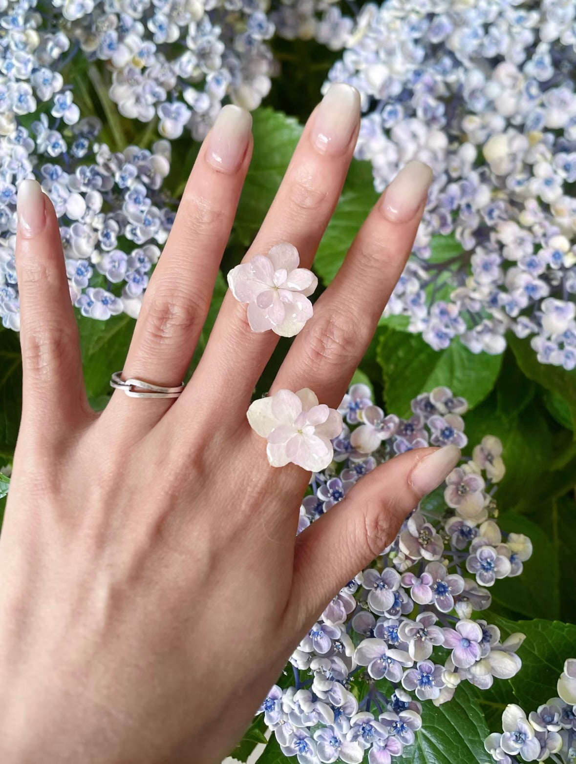 Cream white and soft pink hydrangea rings with resin petals worn on hand by Terra Decode