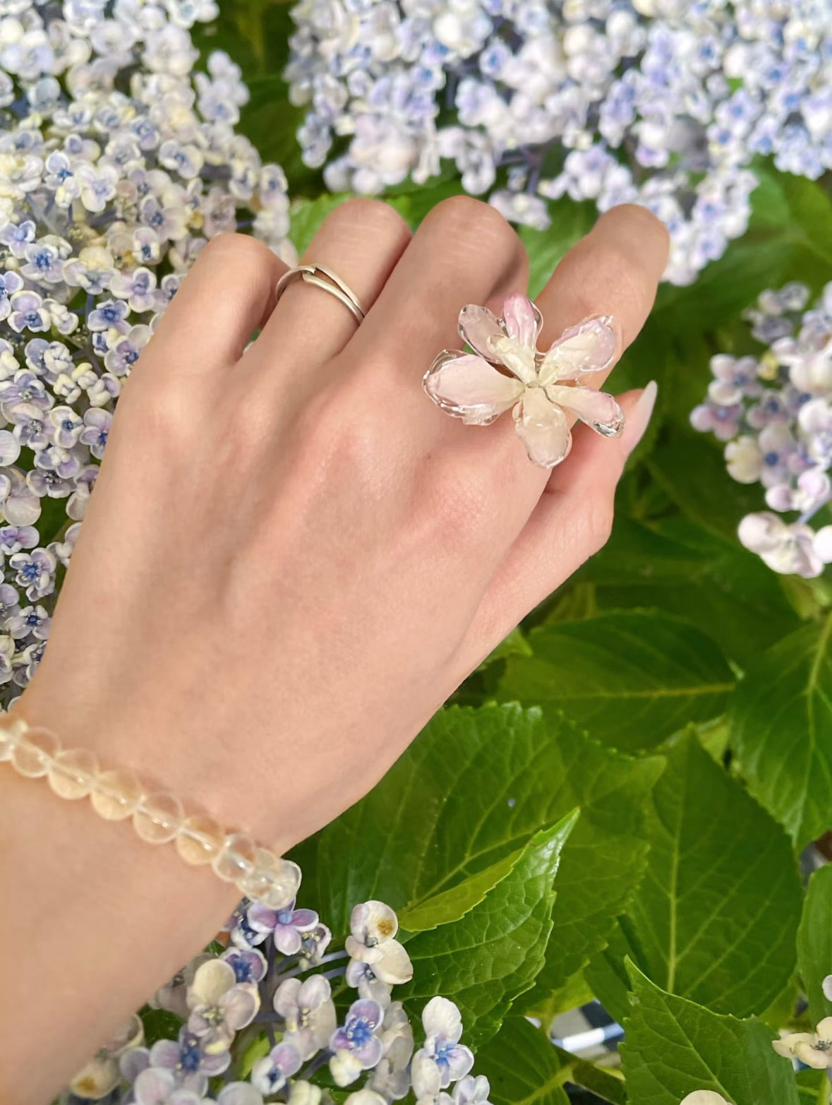 Cream white hydrangea ring with translucent resin petals worn among hydrangea leaves by Terra Decode