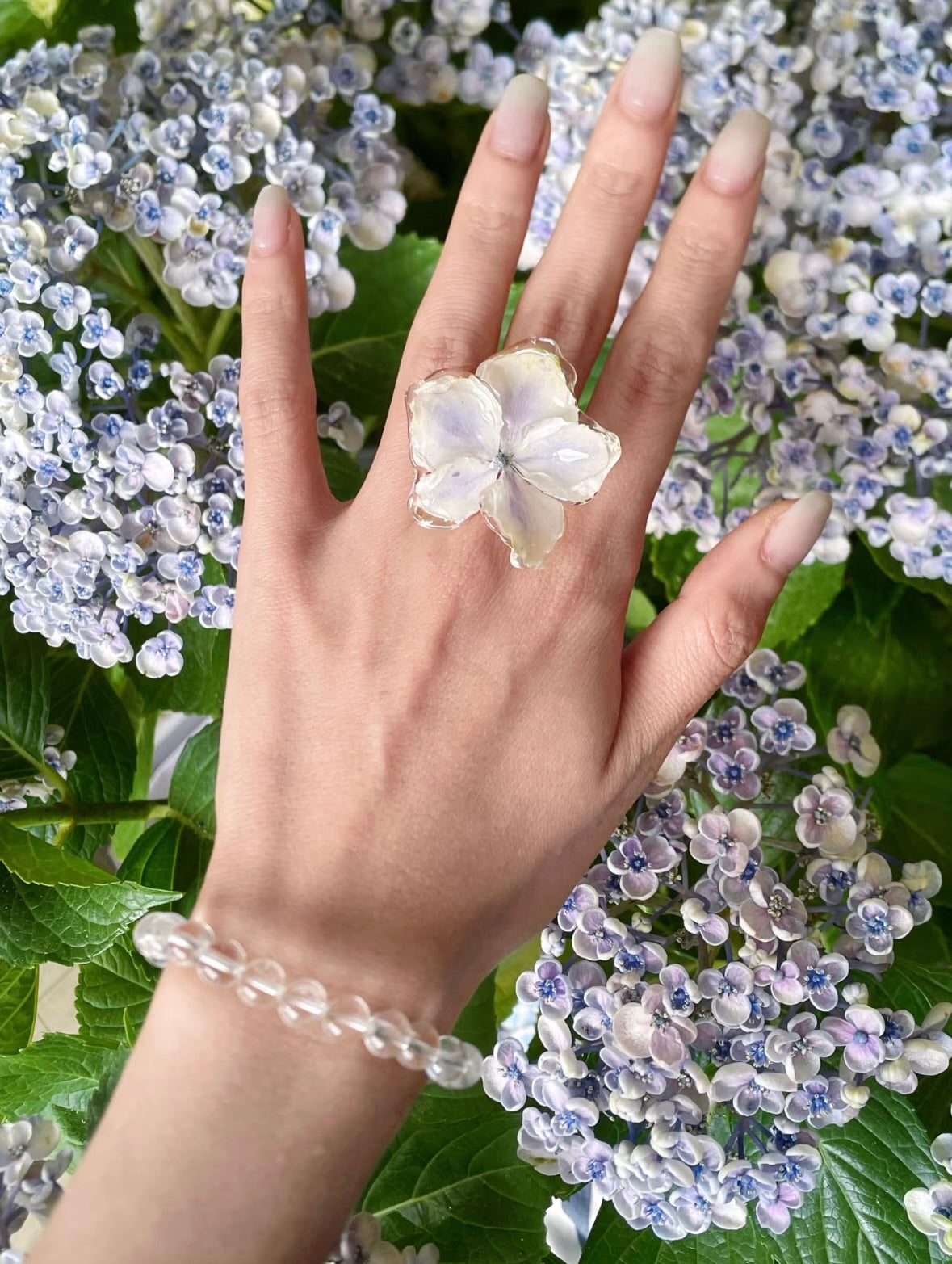 Lavender hydrangea ring with translucent resin petals worn among garden hydrangeas by Terra Decode