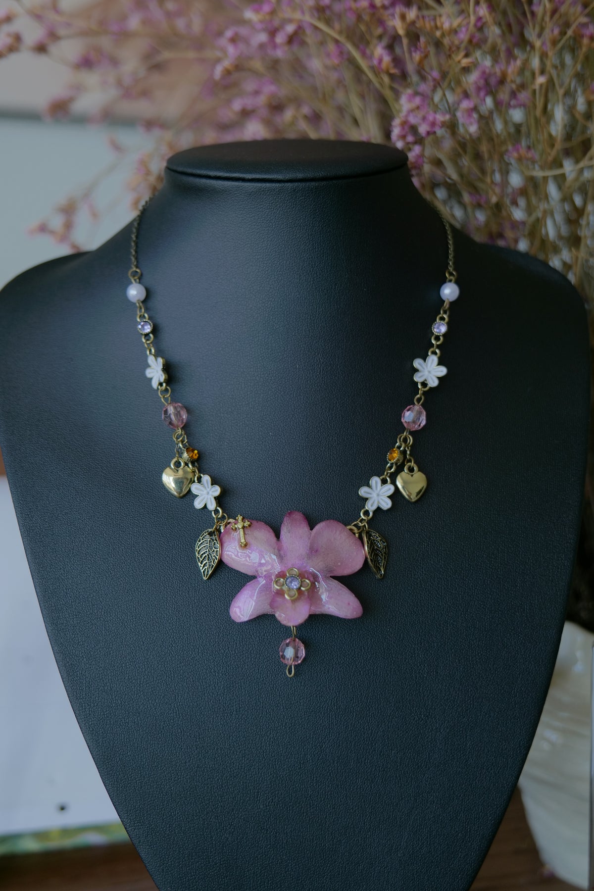 Antique-gold heart, flower and leaf charm details on the Dendrobium necklace