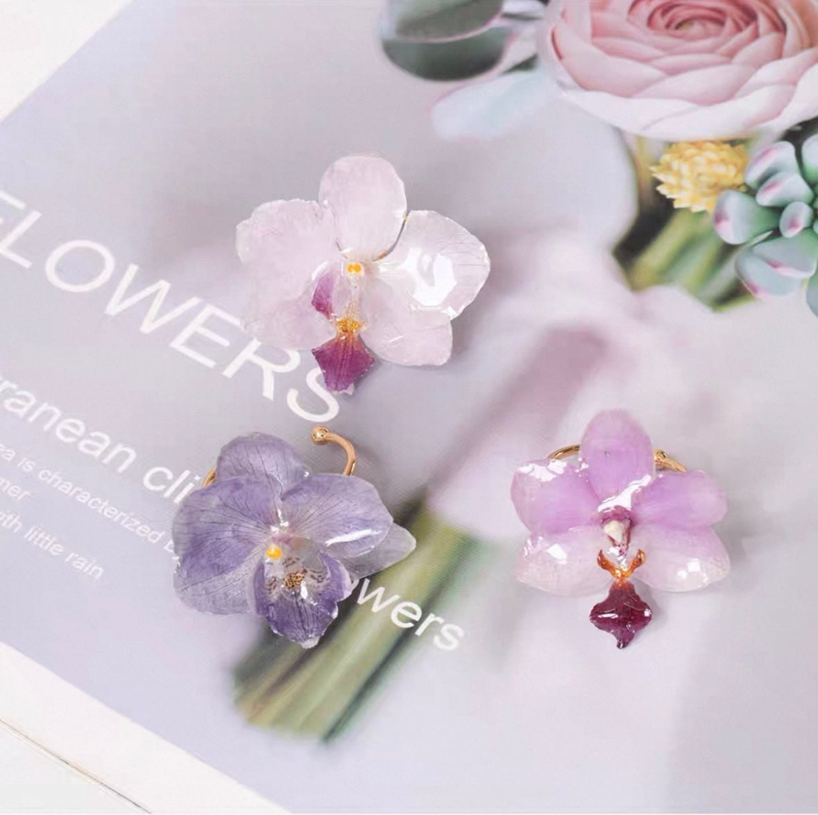Soft purple orchid ring variations with resin petals on a soft styling surface by Terra Decode