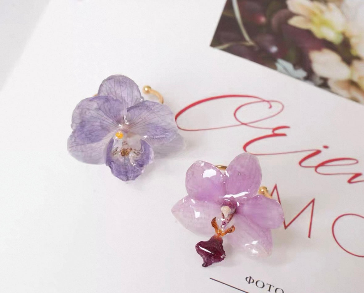 Soft purple orchid ring variations with resin petals on an editorial card by Terra Decode