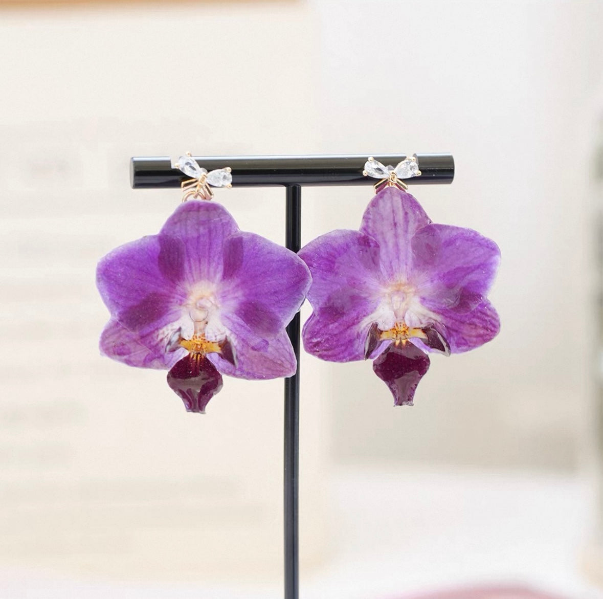 Purple teardrop orchid earrings with resin petals on a black display stand by Terra Decode