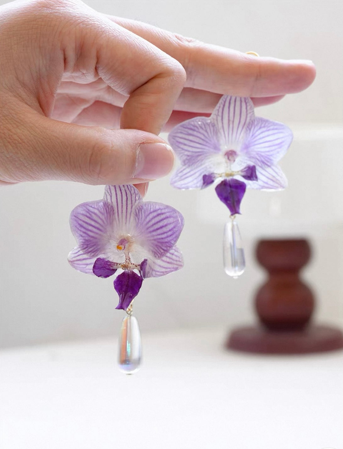 Purple teardrop orchid earrings with resin petals held in hand by Terra Decode
